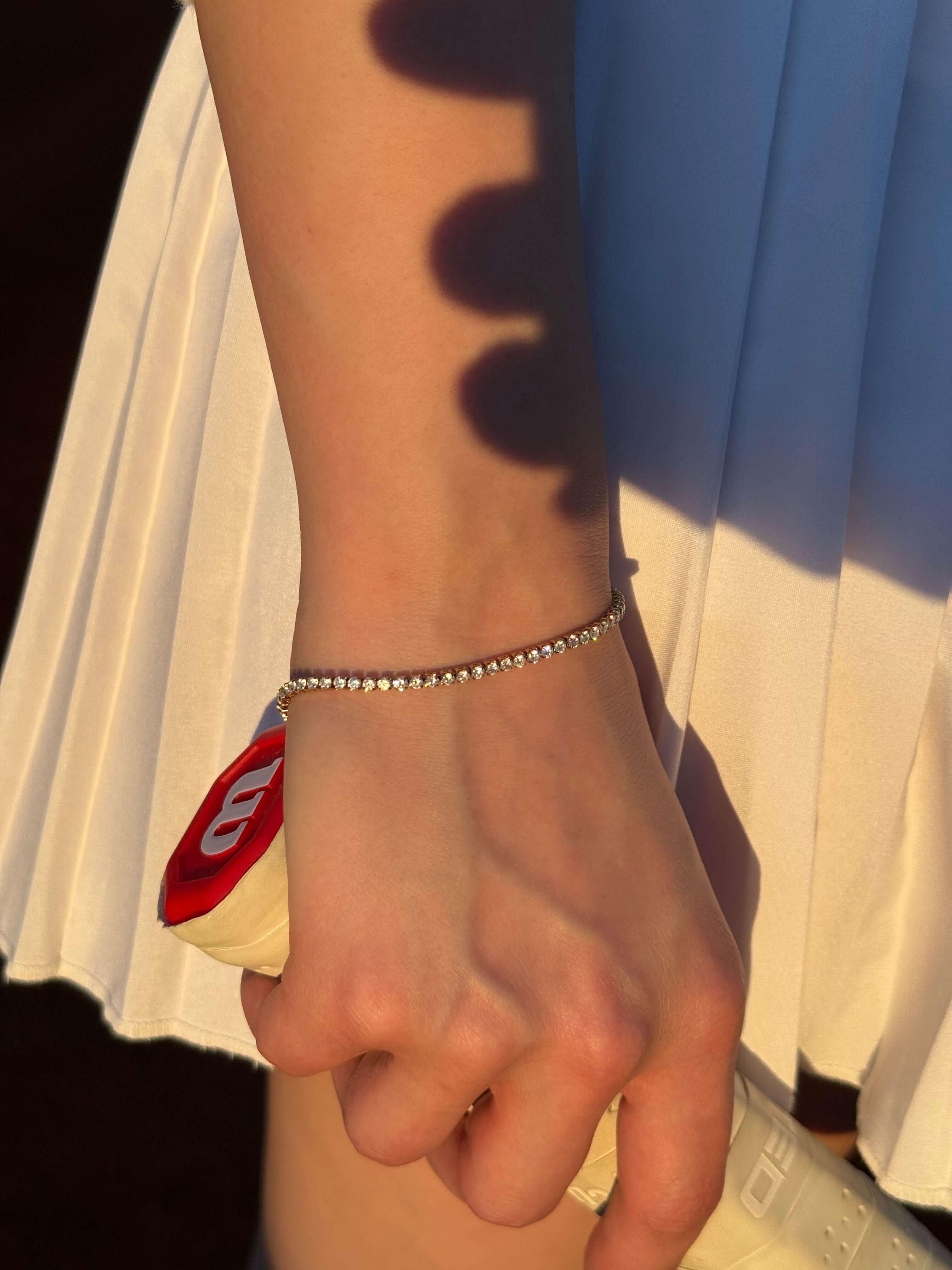 Тенис гривна с 18К златно покритие, носена на ръка, с тенис ракета на фона.