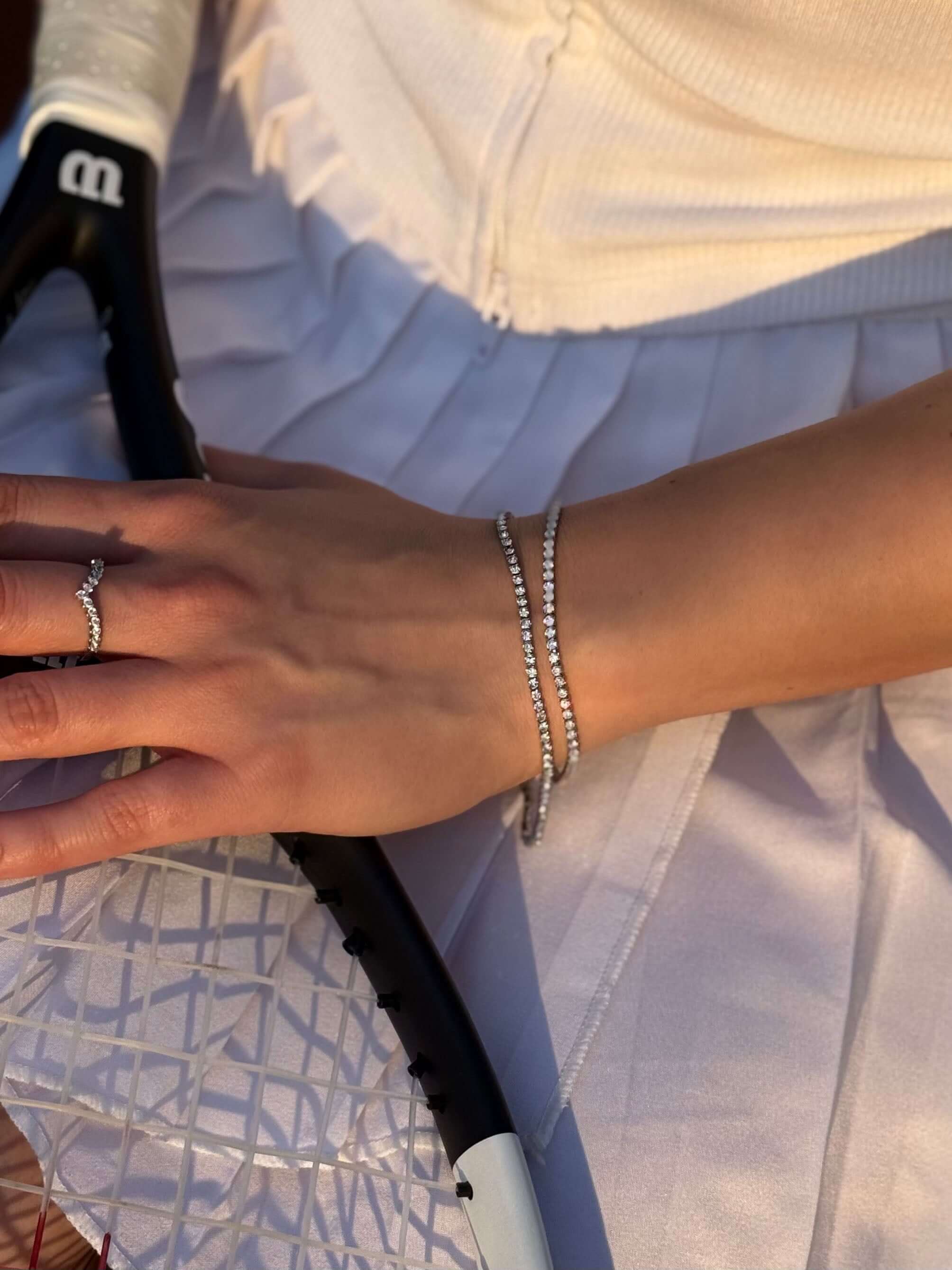 Гривна на ръката с тенис ракета на фона, изработена от неръждаема стомана и с елегантен дизайн.