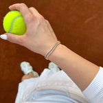 Длан, държаща тенис топка, с тенис гривна от неръждаема стомана и 18К златно покритие.
