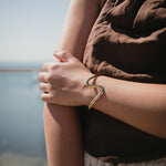 Златиста гривна Wave с 18К златно покритие, носена на ръка, идеален аксесоар за лятото.