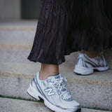 Нови спортни обувки New Balance в комбинация с дълга, plisирана пола, стъпала на стълби.