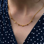 Двойно колие от медицинска стомана с 16к златно покритие и кубчета, носено върху синя риза с бели точки.