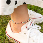 Бохо гривна за глезен с цветен конец и мъниста в лятна обстановка на зелена трева.