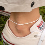 Лека гривна за глезен с цветни мъниста, носена с удобни мокасини на трева.