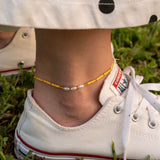 Бохо гривна за глезен с жълти мъниста и перли, носена с бели кеди на зелена трева.