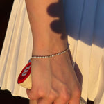 Тенис гривна с 18К златно покритие, носена на ръка, с тенис ракета на фона.