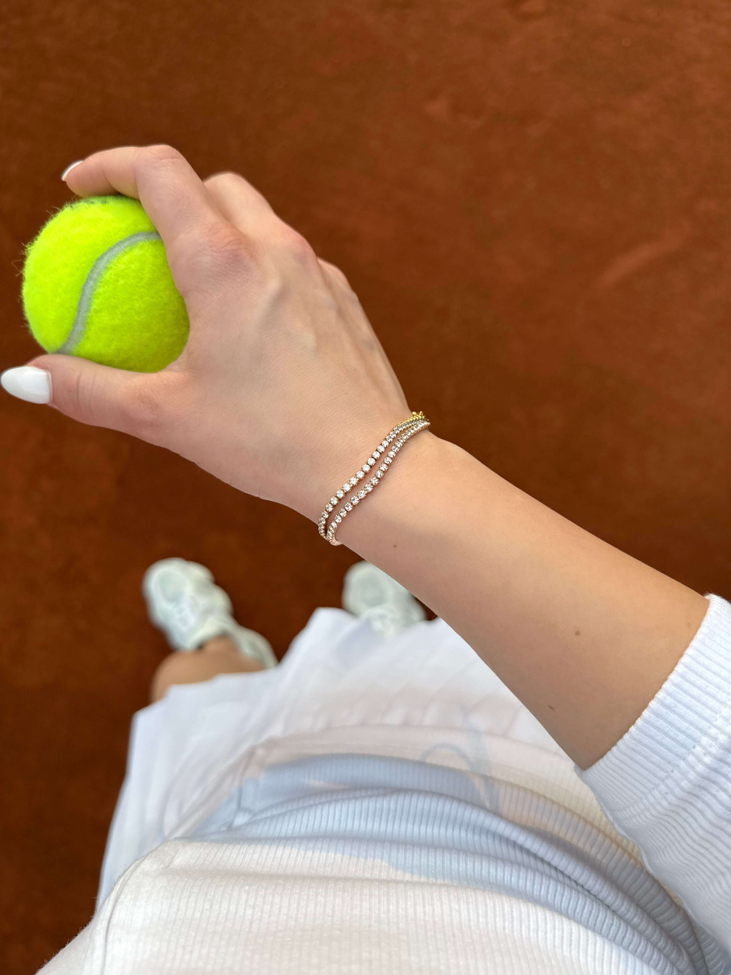 Длан, държаща тенис топка, с тенис гривна от неръждаема стомана и 18К златно покритие.