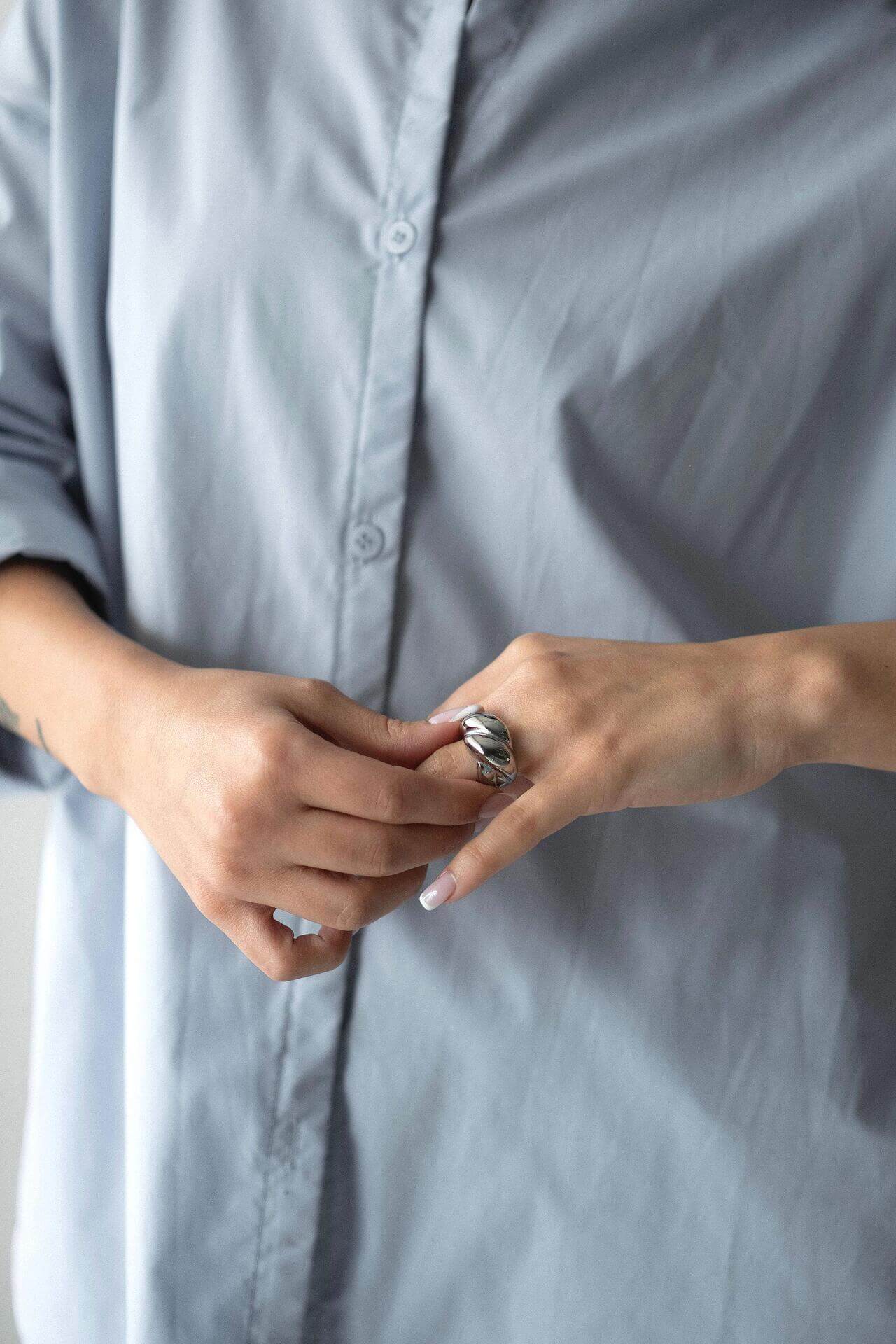 Woman wearing a chunky ring with 18K gold plating over a pale blue shirt, showcasing stylish jewelry.
