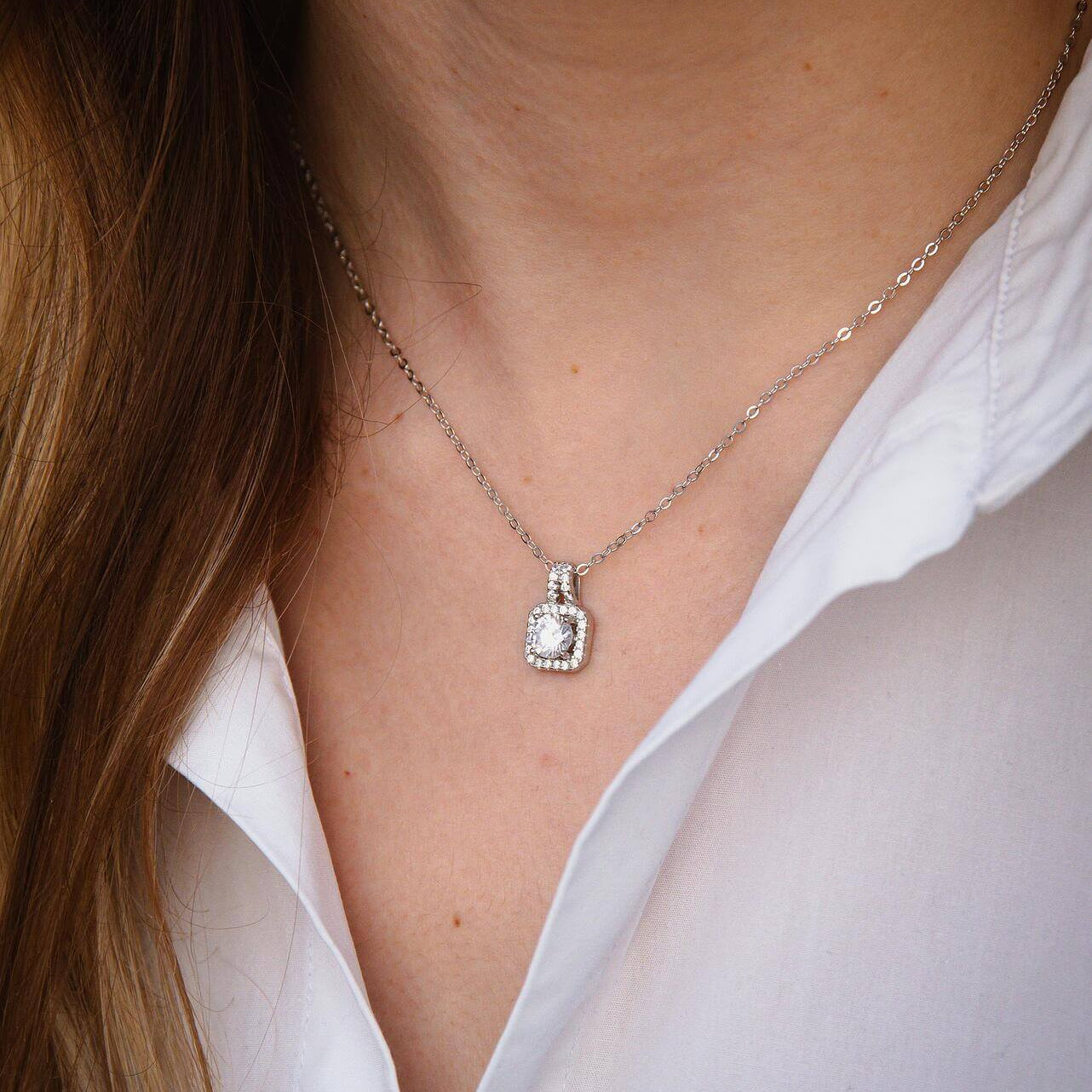 Елегантно сребърно колие с блестящи камъни, носено на жена с бяла риза.