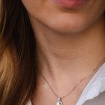 Елегантно сребърно колие с блестящ камък, носено от жена с минималистичен стил и облекло.