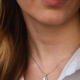 Елегантно сребърно колие с блестящ камък, носено от жена с минималистичен стил и облекло.