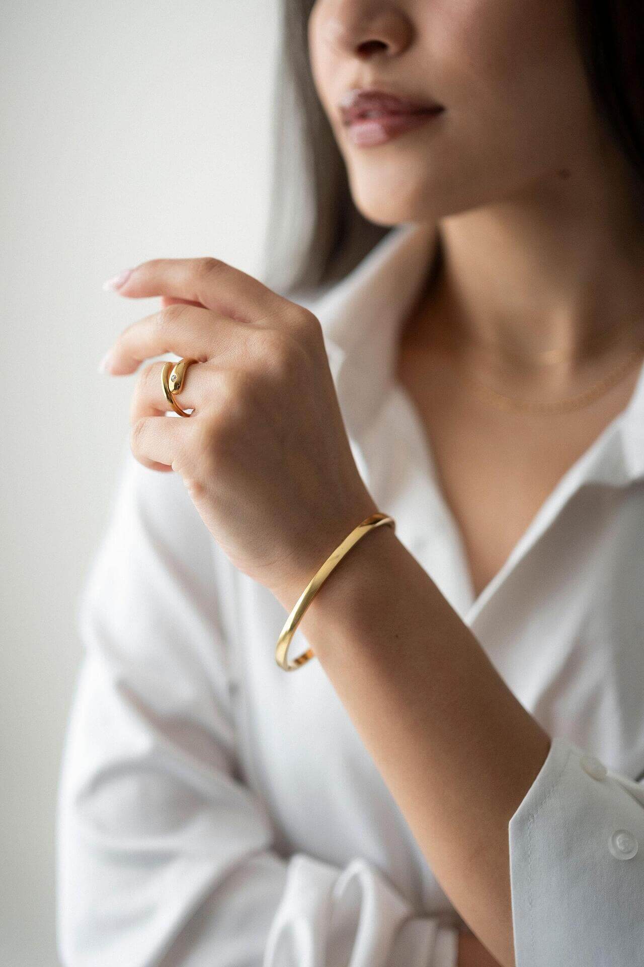 Woman wearing Ayra bracelet with 18K gold plating and stylish ring, showcasing elegant jewelry.