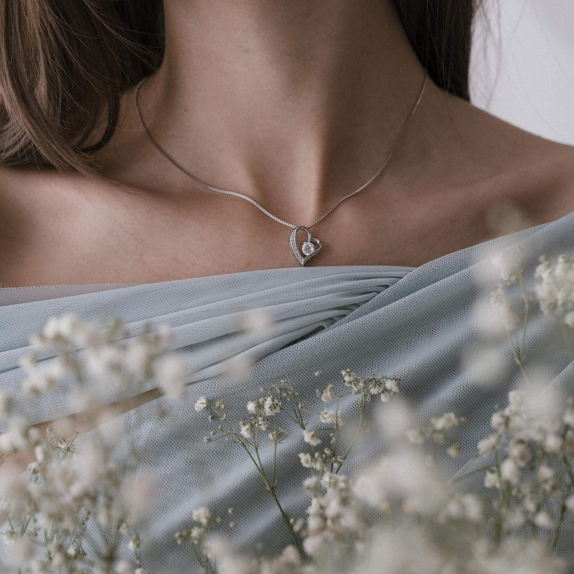 Сребърно колие с форма на сърце S925, носено от жена, с флорален фон.