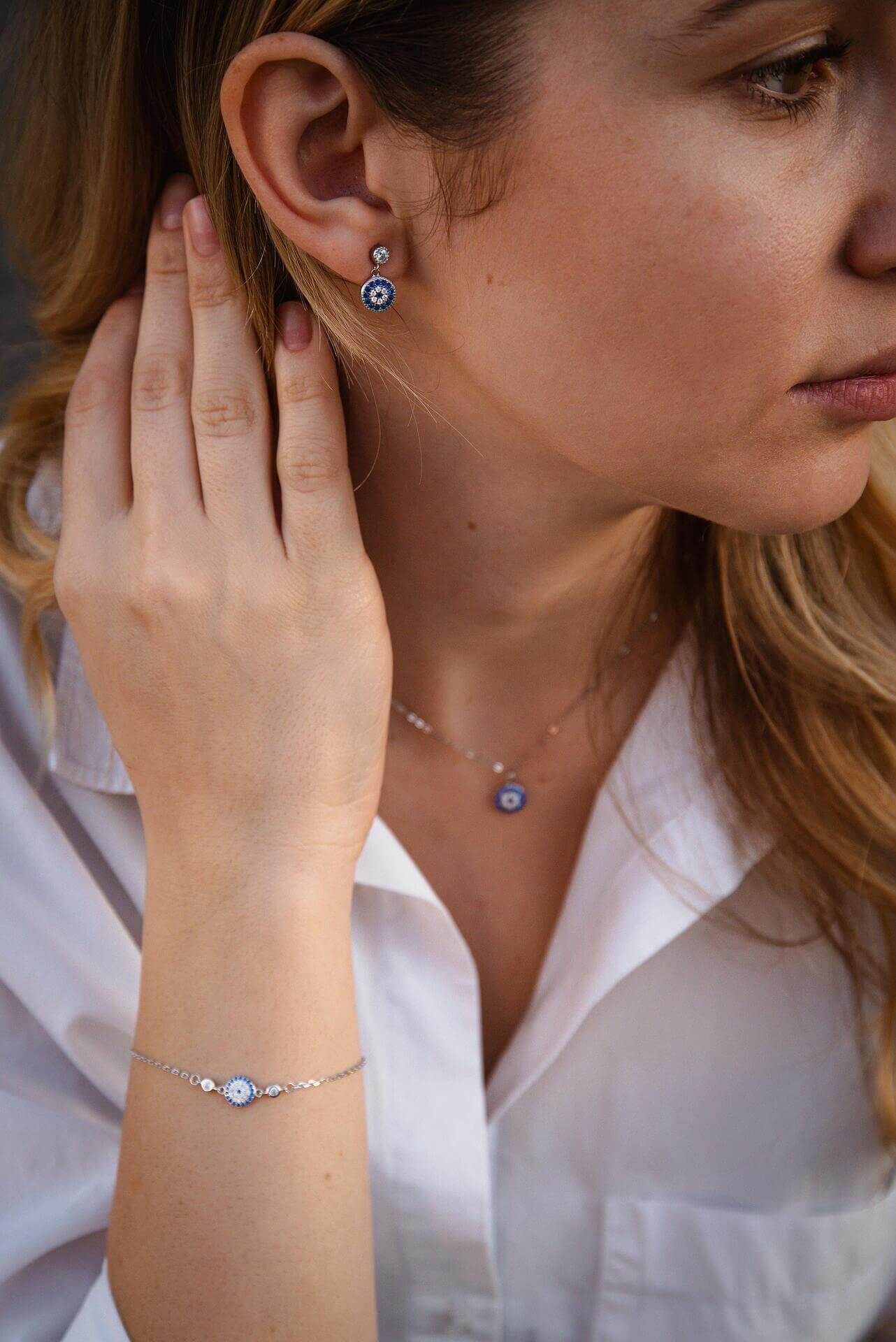 Млада жена носи сребърен комплект Хамса - обеци, гривна и колие, съчетаващи стил и защита.