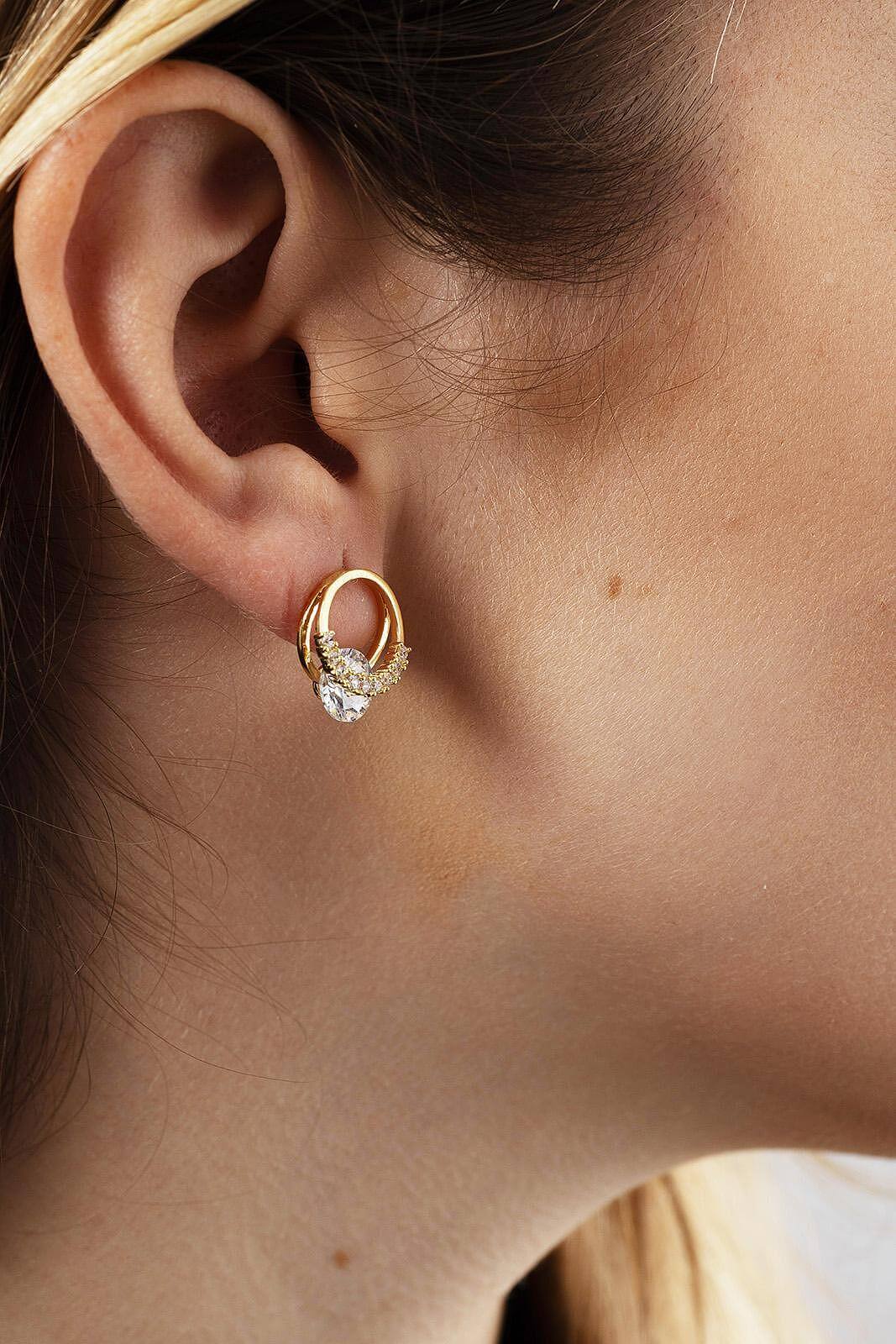 Обeци с блестящ камък в златист цвят, носени от жена, подчертаващи елегантността и стилa.