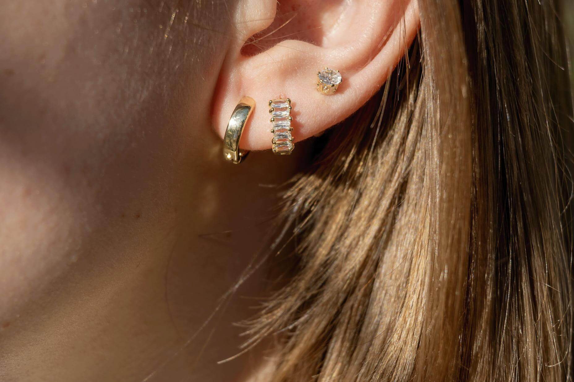 Close-up of stylish gold earrings on a woman's ear, showcasing a trio of piercings with shimmering designs.