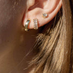 Close-up of stylish gold earrings on a woman's ear, showcasing a trio of piercings with shimmering designs.
