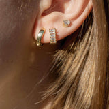 Close-up of stylish gold earrings on a woman's ear, showcasing a trio of piercings with shimmering designs.