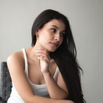 Woman wearing Liquid Drop earrings with 18K gold plating, posing thoughtfully in a stylish setting.