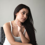 Woman wearing Liquid Drop earrings with 18K gold plating, posing thoughtfully in a stylish setting.