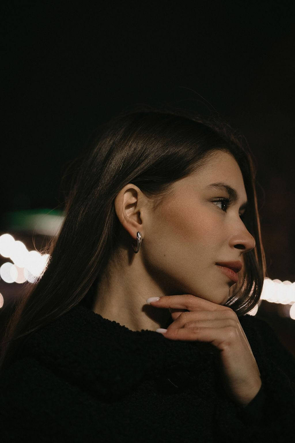 Жена с дълга коса, носеща обеци V-Shape в тъмен фон с светлини на заден план.
