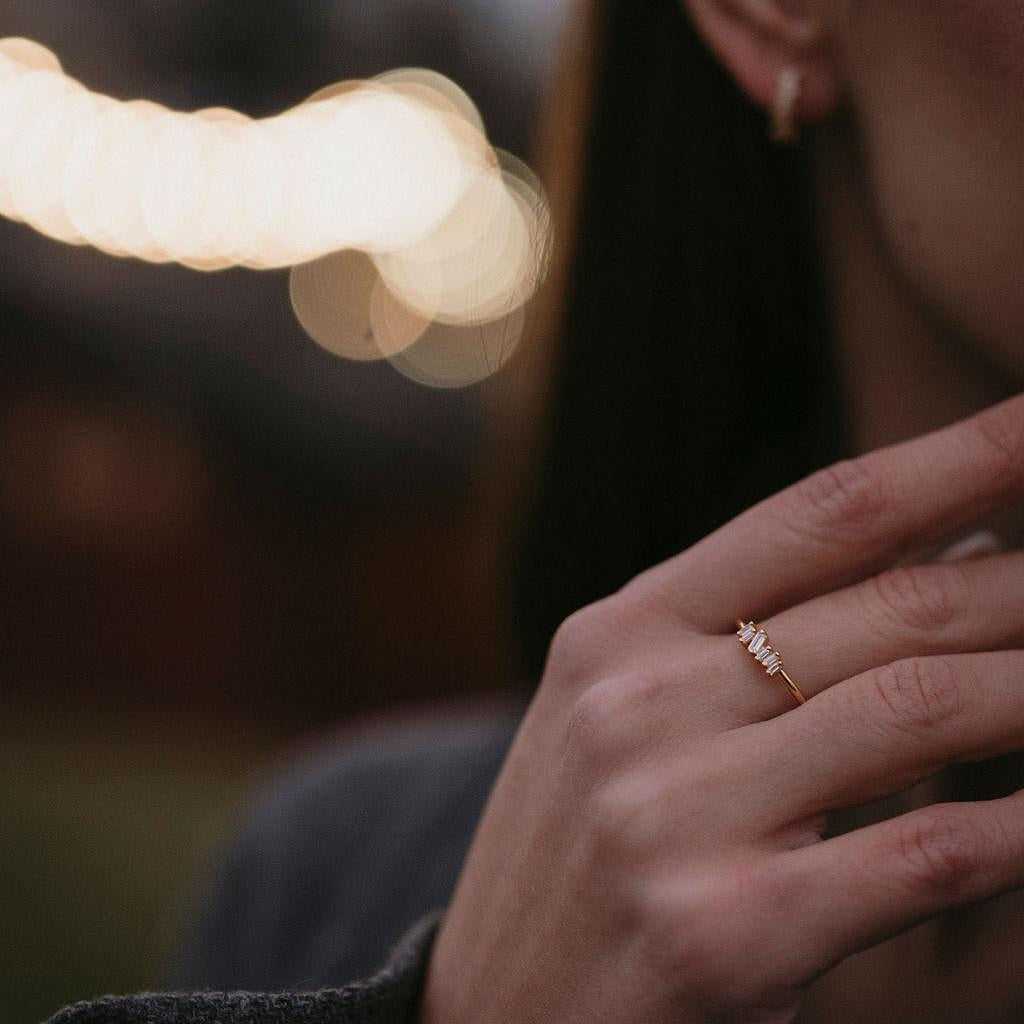 Сребърен пръстен с диамант и цирконий, носен от жена на фона на размити светлини.
