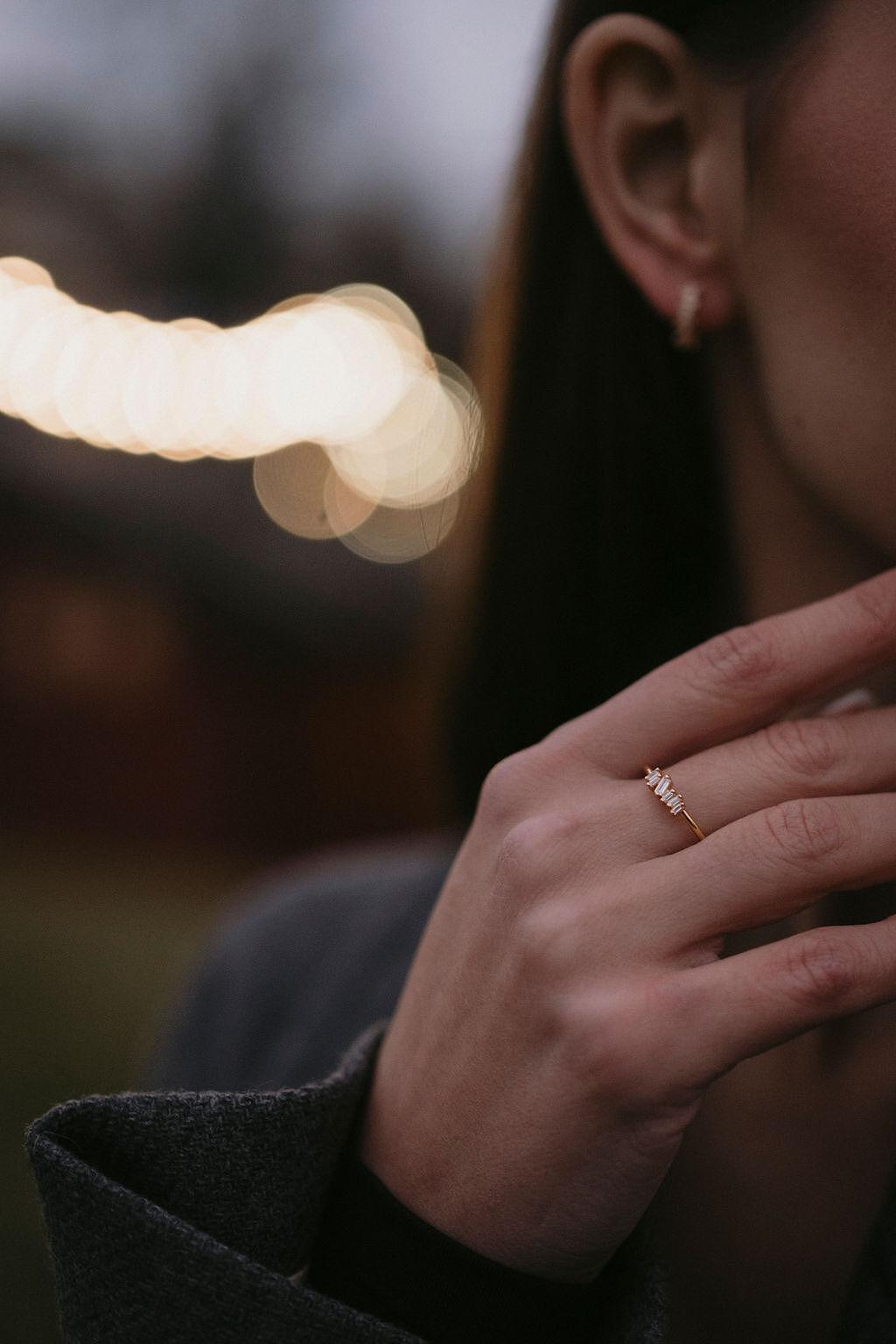 Сребърен пръстен с диамант и цирконий, носен от жена на фона на размити светлини.