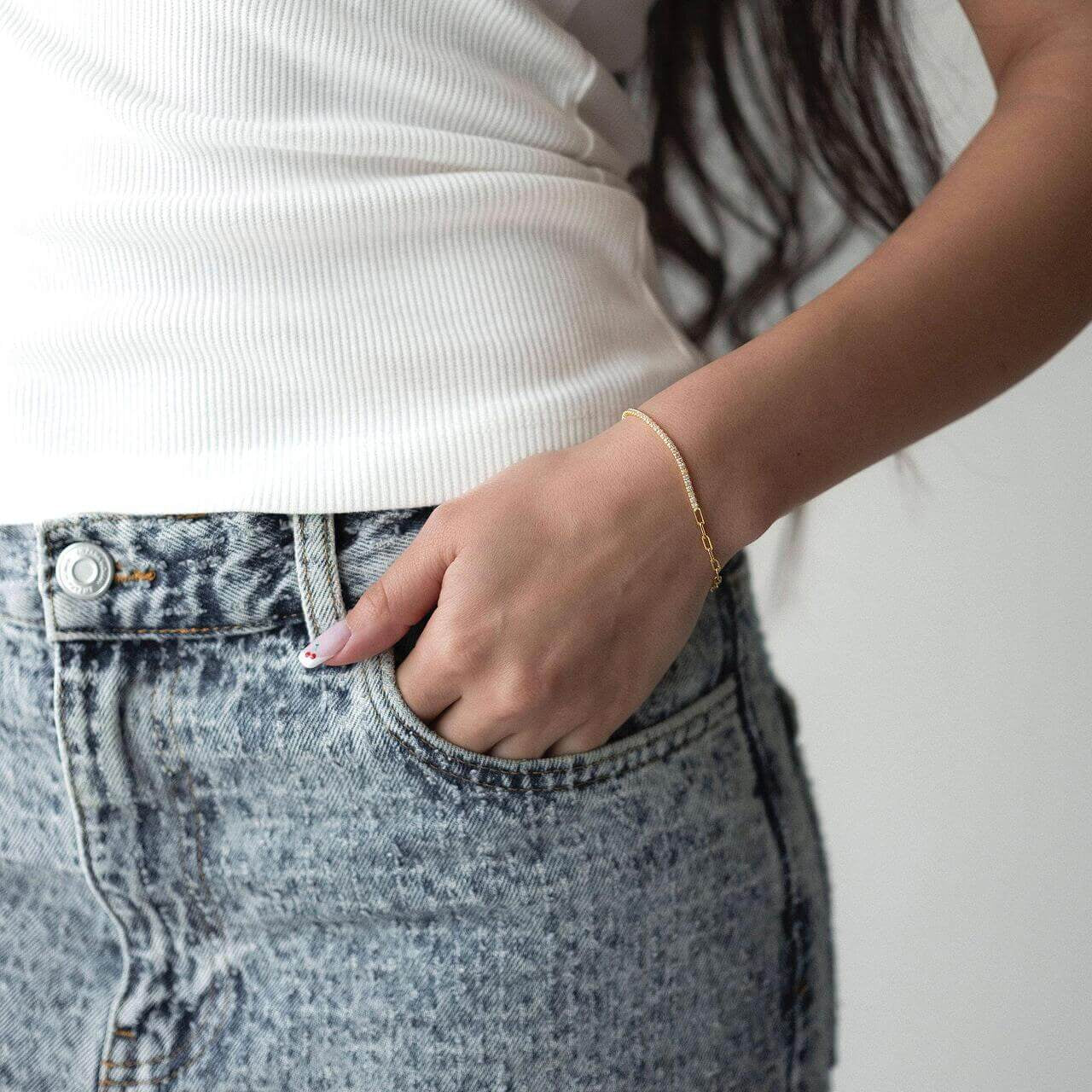 Жена с бели потници и дънки, носеща сребърна гривна с 18K златно покритие.