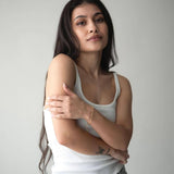 Stylish young woman wearing a white tank top and jeans, showcasing a delicate silver bracelet against a neutral background.