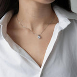 Сребърно колие S925 с цирконов камък, носено върху бяла риза, близък план на шията.