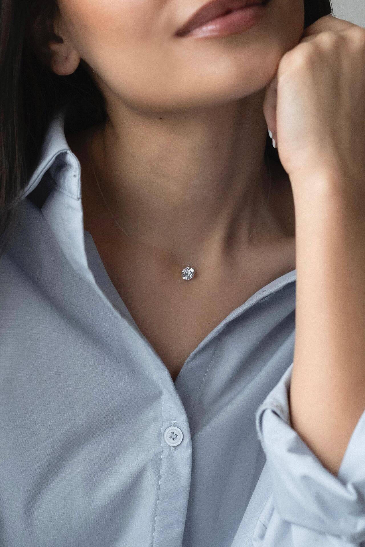 Сребърно колие с циркон на фона на жена в светло синя риза, акцентиращо на елегантност и стил.