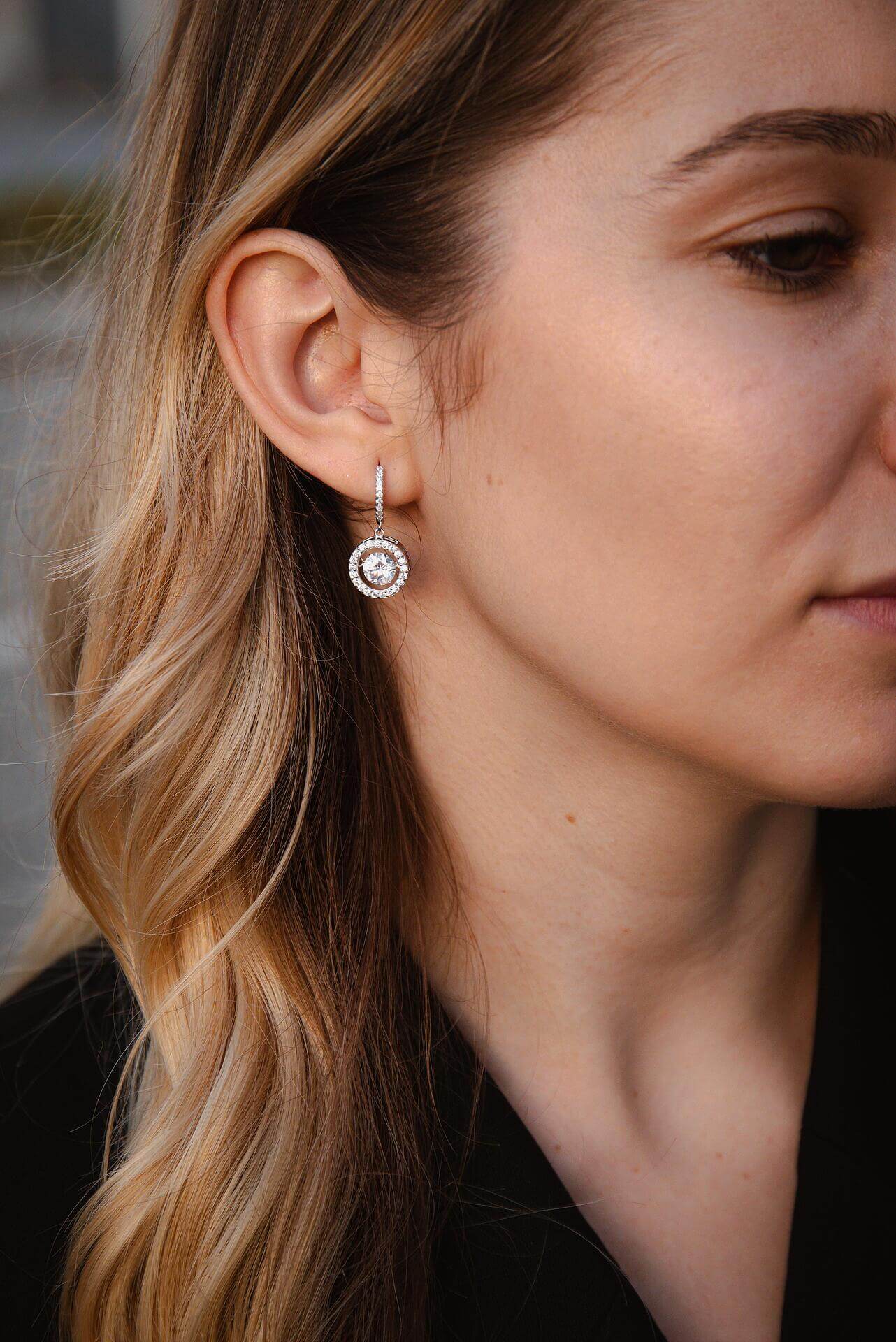 Висящи обеци с блестящи камъни и сребро S925, носени от жена с дълга коса.