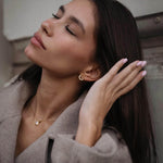 Модерна жена с дълга коса, носеща златисти обеци "Хибрид" с 18K златно покритие.