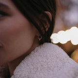 Златисти обеци с многонюансни кристали, носени от жена в уютно облекло, с ненатрапчив блясък.