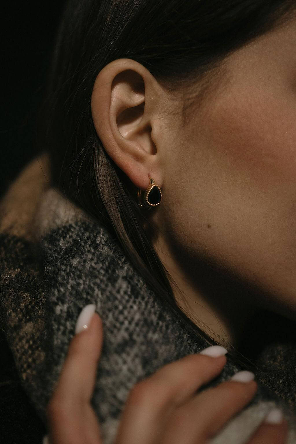 Златисти обеци с кристали, носени от жена с елегантен шал, подчертаващи модния стил.