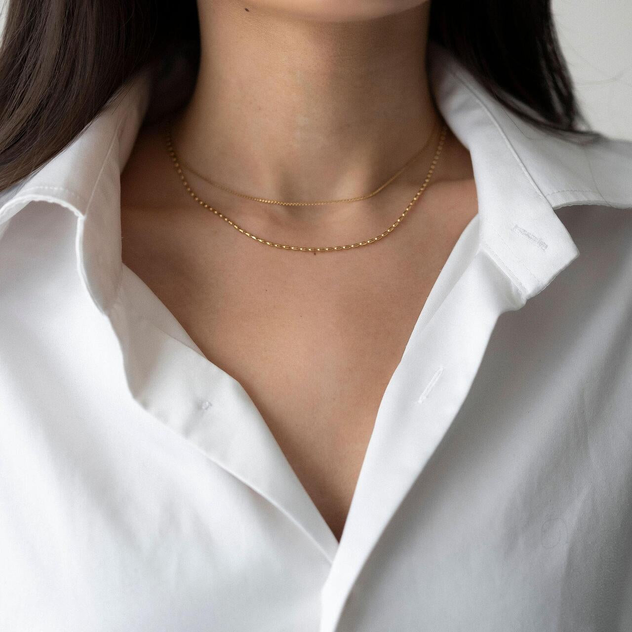 Златисто двойно колие Elara на нежна жена, облечена в бяла риза, изтъкваща елегантния дизайн.