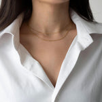 Златисто двойно колие Elara на нежна жена, облечена в бяла риза, изтъкваща елегантния дизайн.