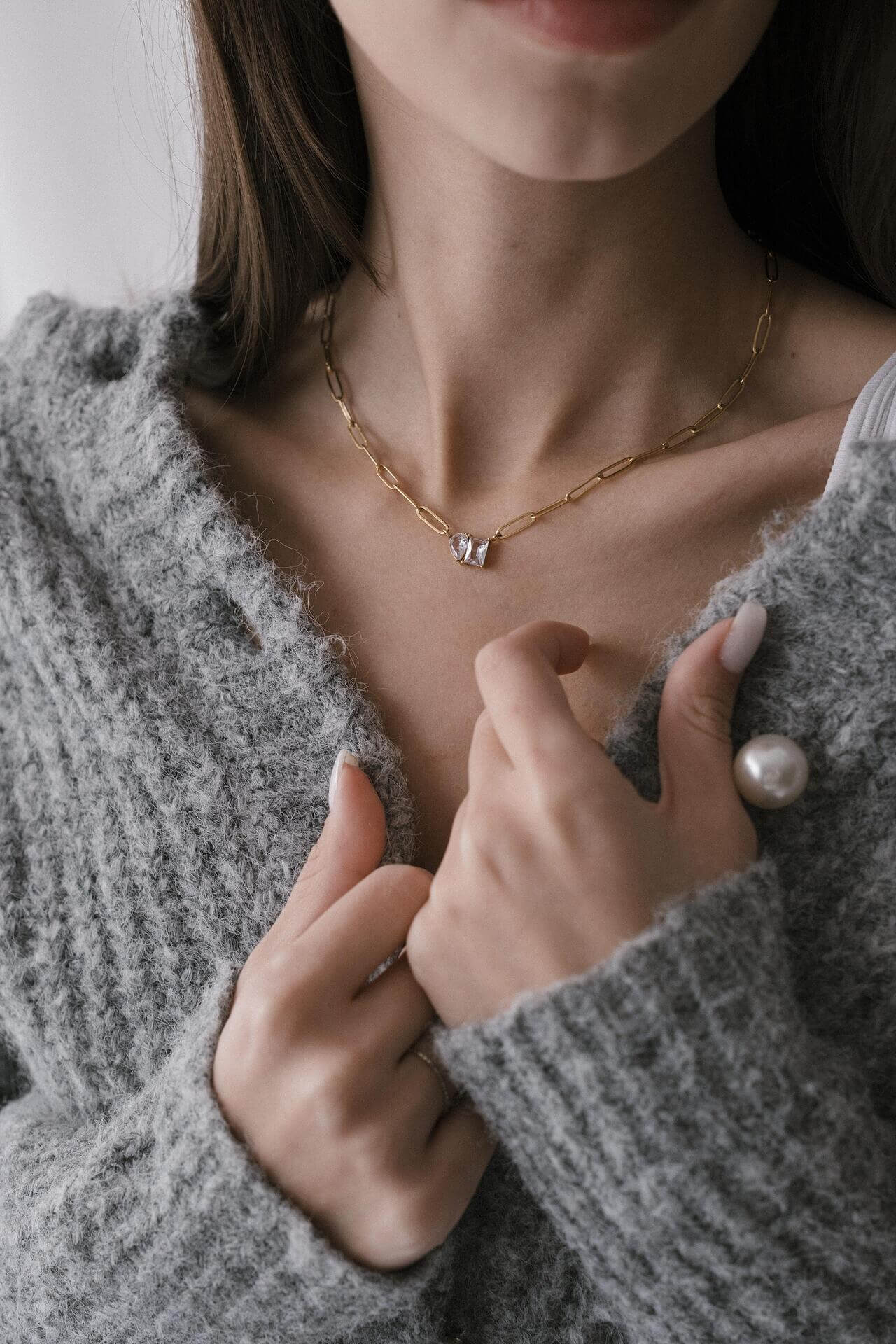 Жена с златисто колие One of a Kind, облечена в сива игла, показваща елегантен стил и индивидуалност.